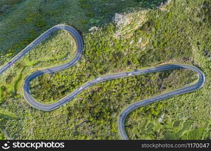 Aerial top view of a winding serpentine road over a a mountain with trees and rocks