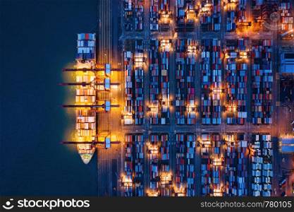 Aerial top view of container cargo ship in the export and import business and logistics international goods in urban city. Shipping to the harbor by crane in Victoria Harbour, Hong Kong City at night.