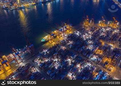 Aerial top view of container cargo ship in the export and import business and logistics international goods in urban city. Shipping to the harbor by crane in Victoria Harbour, Hong Kong City at night.