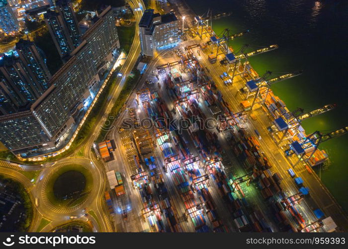 Aerial top view of container cargo ship in the export and import business and logistics international goods in urban city. Shipping to the harbor by crane in Victoria Harbour, Hong Kong City at night.