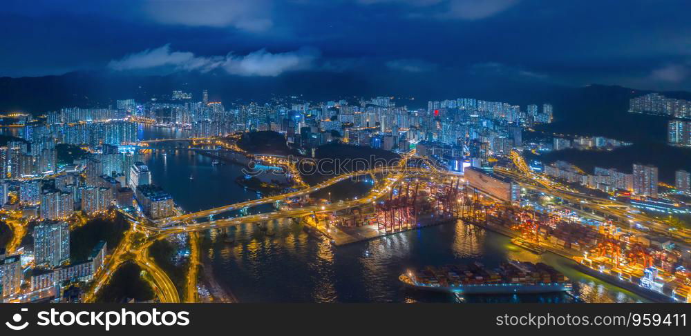 Aerial top view of container cargo ship in the export and import business and logistics international goods in urban city. Shipping to the harbor by crane in Victoria Harbour, Hong Kong City at night.