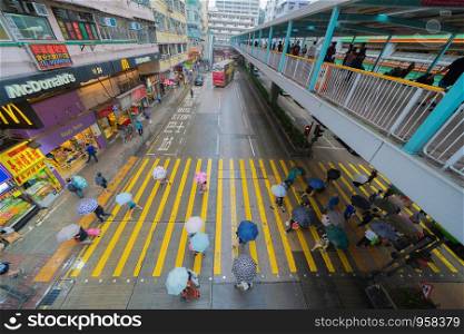 Aerial top view of crowd of people with umbrellas walking on street over zebra crossing or pedestrian crossing while raining. Traffic road in busy urban city. Hong Kong Downtown, Republic of China.