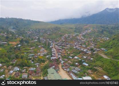 Aerial top view of immigrant refugees residential village houses in countryside, rural area. Local community houses in urban town near natural forest on mountain hills, Tak, Thailand. Evacuation.