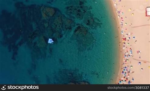 Aerial top view of people sunbathing and swimming on famous white beach in Spain, Catalonia