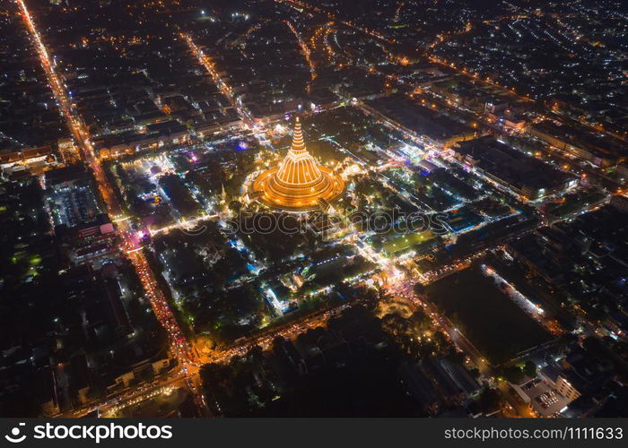 Aerial top view of Phra Pathommachedi temple at night. The golden buddhist pagoda with residential houses, urban city of Nakorn Pathom district, Thailand. Holy Thai architecture.