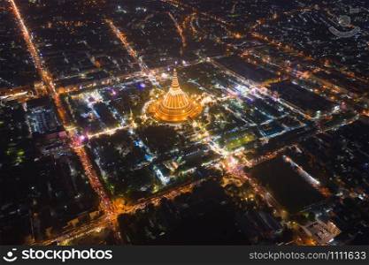 Aerial top view of Phra Pathommachedi temple at night. The golden buddhist pagoda with residential houses, urban city of Nakorn Pathom district, Thailand. Holy Thai architecture.