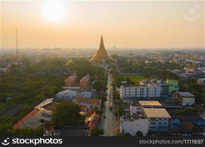 Aerial top view of Phra Pathommachedi temple at sunset. The golden buddhist pagoda with residential houses, urban city of Nakorn Pathom district, Thailand. Holy Thai architecture.
