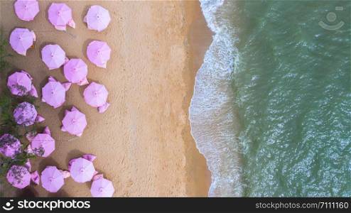 Aerial top view on the sandy beach. Pink umbrellas, sand, beach chairs and sea waves.
