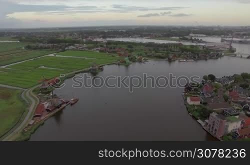 Aerial - Township with old windmills, river with sailing boat and green fields, Netherlands