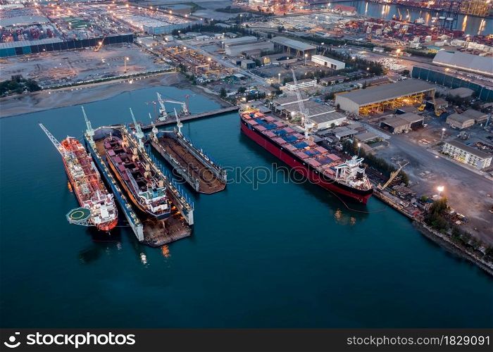 Aerial view Container ship repair in shipyard at twilight over lighting . Can use for shipping or transportation concept.