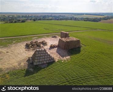 Aerial view from a drone tractor folding a pile of hay in stacks on a green field on a sunny day. Agribusiness concept. Green field with large haystacks and tractor on a sunny day. Aerial view from the drone