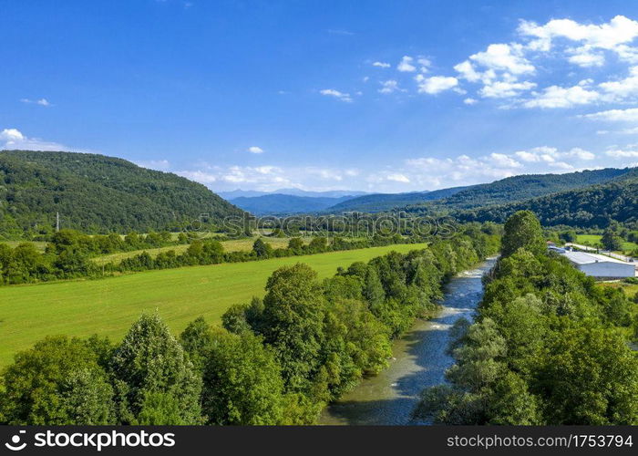 Aerial view from drone of the vast green landscape with river, hills and blue sky