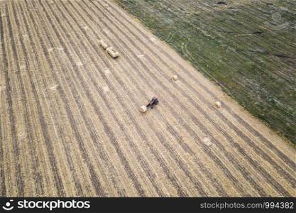 Aerial view from drone to the tractor collect bales of hay after harvesting on a wheat field.