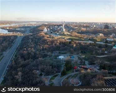 Aerial view from the drone to the Dnieper River, the Motherland Monument, Spivoche Pole, parks, historical and modern architecture of city in Kiev, Ukraine in the summer sunset.. Amazing sityscape on the right banks of the Dnieper, the Motherland Monument, Spivoche Pole in Kiev, Ukraine.