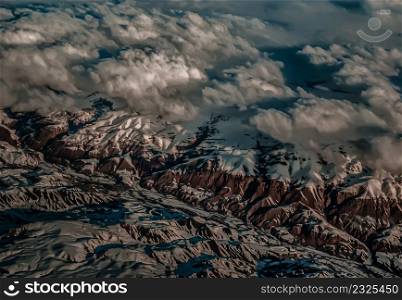 Aerial view from the plane of hills snow and mountains landscape with shadows of sunlight and clouds covered beautifully. Above the clouds, Snow capped mountain, No focus, specifically.