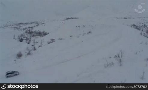 Aerial view of a car getting through the heavy deep snow on mountain road on dull winter day