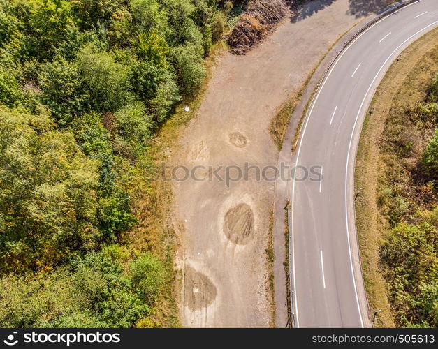 Aerial view of a lonely asphalted country road in the Harz Mountains with a neighbouring forest and the basin of a dam.