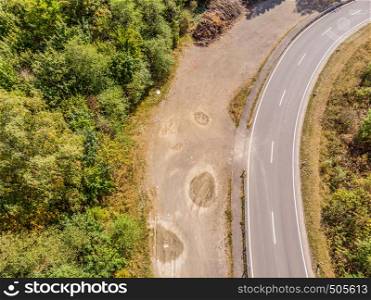 Aerial view of a lonely asphalted country road in the Harz Mountains with a neighbouring forest and the basin of a dam.