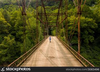 Aerial view of a senior woman walking her dog across the historic metal truss Jenkinsburg Bridge near Morgantown over Cheat River. Drone view of senior woman walking dog across Jenkinsburg Bridge over Cheat River