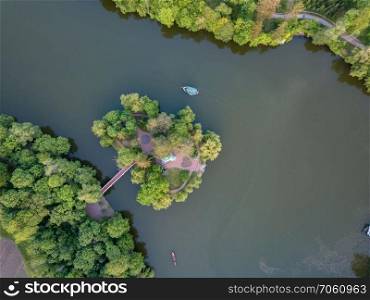 Aerial view of a small lake in the middle of a forest and an island with a bridge among a huge green forest. A small boat is going along the water. Photo by drone. small lake in the middle of a forest and an island with a bridge, top view