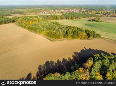 Aerial view of a small piece of forest between fields and meadows behind a village in northern Germany.