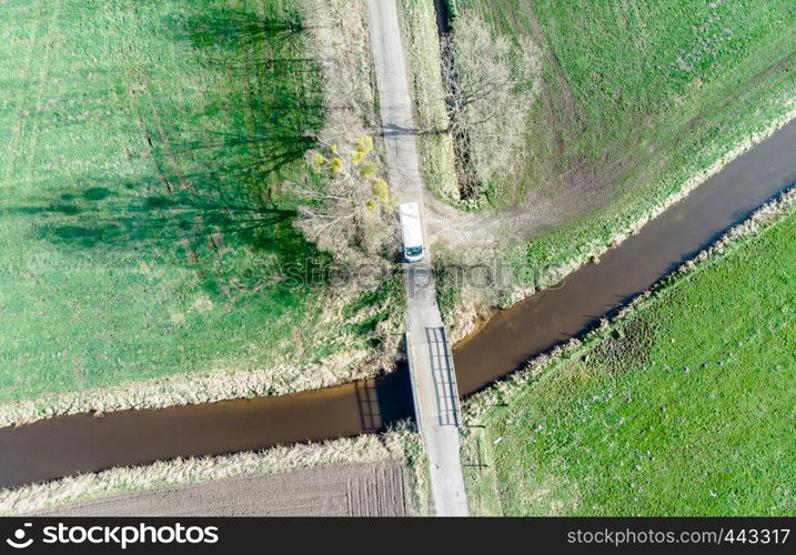 Aerial view of a stream flowing through meadows and fields under a little bridge, made with drone