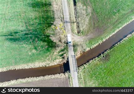 Aerial view of a stream flowing through meadows and fields under a little bridge, made with drone