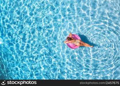 Aerial view of a young woman swimming with pink swim ring in blue sea with school of fish at sunset in summer. Tropical landscape with girl, clear water, sandy beach in Greece. Top view. Travel