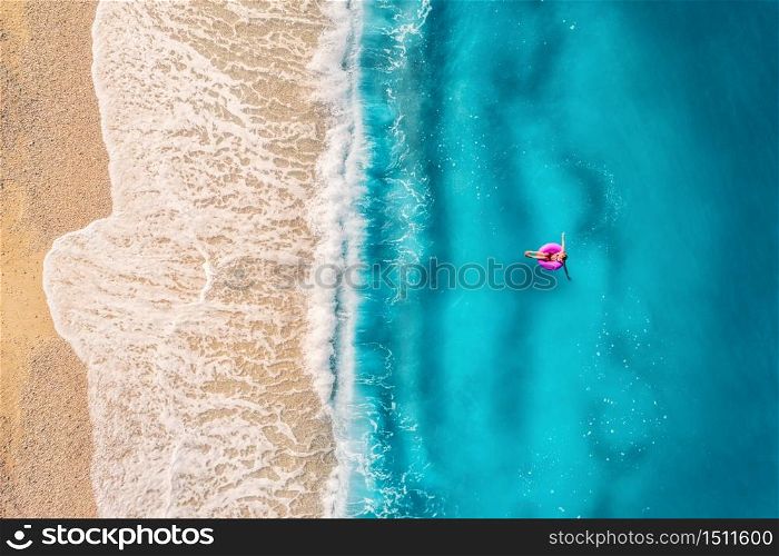 Aerial view of a young woman swimming with the donut swim ring in transparent blue sea with waves at sunset in summer in Turkey. Tropical landscape with girl, azure water, sandy beach. Top view