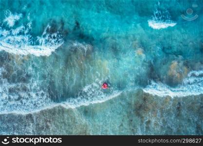 Aerial view of a young woman swimming with the donut swim ring in the clear blue sea with beautiful waves at sunset in summer. Tropical aerial landscape with girl, azure water. Top view. Travel