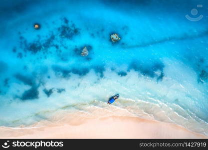 Aerial view of alone fishing boat in blue transparent water at sunset in summer. Top view of boat, yacht, white sandy beach in Zanzibar. Travel. Tropical seascape with sailboat, sea. View from above. Aerial view of the fishing boat in clear blue water at sunset