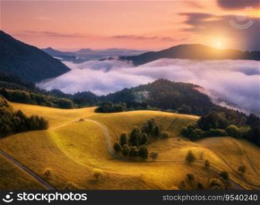 Aerial view of alpine meadows and mountains in low purple clouds at sunrise in autumn. Top drone view of hills, yellow grass and trees in fog, colorful sky in fall. Slovenia. Nature. Mountain valley 