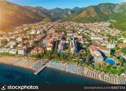 Aerial view of beautiful city. Aerial view of beautiful city, sandy beach with chaise-lounges, mountains, green trees, hotels, buildings, pool, at sunset in Icmeler, Turkey. Summer cityscape Top view from drone. Architecture