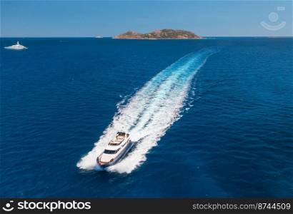 Aerial view of beautiful floating luxury yacht in blue sea at sunset in summer. Sardinia island, Italy. Top view of speed boat, sea coast, transparent water. Travel. Tropical landscape. Yachting 