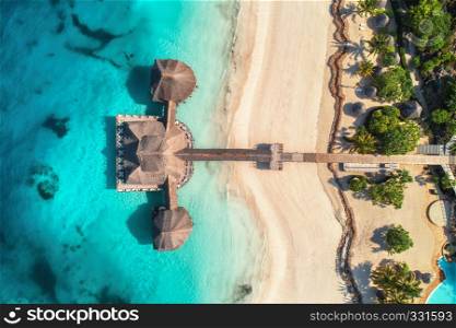 Aerial view of beautiful hotel in Indian ocean at sunrise in summer. Zanzibar, Africa. Top view. Building on the sea. Aerial landscape with wooden hotel, clear azure water, sandy beach. Luxury resort