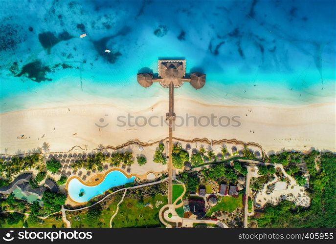 Aerial view of beautiful hotel in Indian ocean at sunrise in summer. Zanzibar, Africa. Top view. Landscape with wooden hotel on the sea, azure water, sandy beach, green trees, pool. Luxury resort