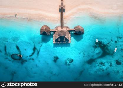 Aerial view of beautiful hotel in Indian ocean at sunset in summer. View from above. Building on the transparent sea. Aerial seascape with wooden hotel, clear azure water, sandy beach. Luxury resort