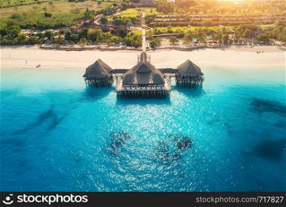 Aerial view of beautiful hotel in Indian ocean at sunset in summer. Zanzibar, Africa. Top view. Landscape with wooden hotel on the sea, blue water, sandy beach, green trees, buildings. Luxury resort. Aerial view of beautiful hotel in Indian ocean at sunset in summer