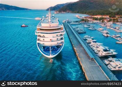 Aerial view of beautiful large white ship at sunset. Cruise ship at harbor. Aerial view of beautiful large white ship at sunset. Colorful landscape with boats in marina bay, sea, colorful sky. Top view from drone of yacht. Luxury cruise. Floating liner