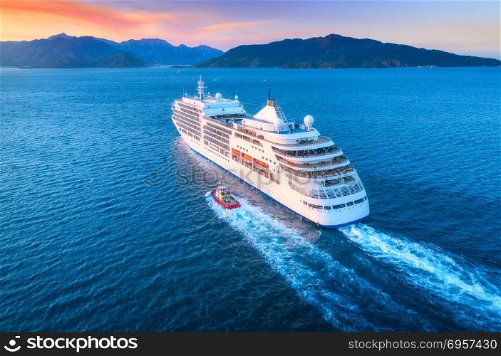 Aerial view of beautiful large white ship at sunset. Cruise ship at harbor. Aerial view of beautiful large white ship at sunset. Colorful landscape with boats in marina bay, sea, colorful sky. Top view from drone of yacht. Luxury cruise. Floating liner