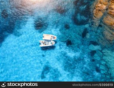 Aerial view of beautiful little boats in blue sea at sunset in summer. Sardinia, Italy. Top drone view of motorboats, ocean with transparent azure water. Travel. Tropical landscape. Yachting. Seascape