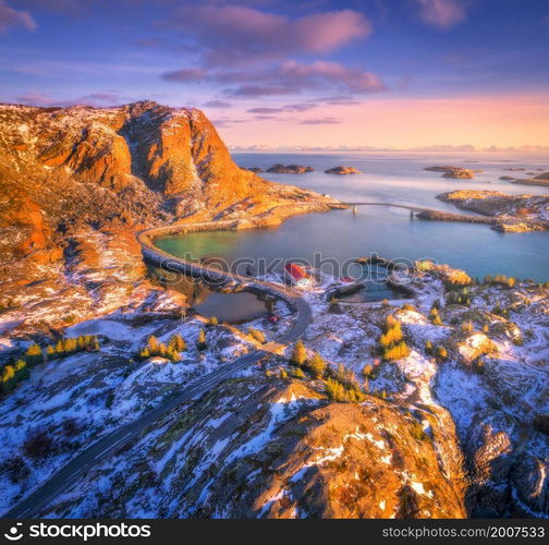 Aerial view of beautiful mountains, bridge, small islands in the sea, road, purple sky at sunset. Lofoten islands, Norway in winter. Top view of road, snowy rocks, stones, sea coast, water. Top view