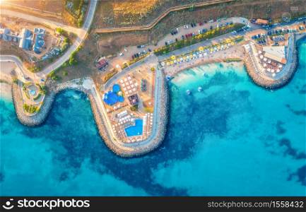 Aerial view of beautiful sandy beach, blue sea, restaurants on the promenade, pool, umbrellas, swimming people in clear water, green trees at sunset in summer. Top view of seafront. Tropical landscape