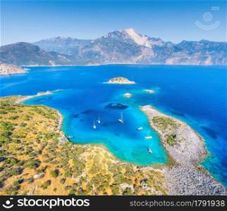 Aerial view of beautiful sea bay, yachts and boats at sunset in summer. Akvaryum koyu in Turkey. Top view of luxury yachts, sailboats, clear blue water, rock, sky, mountain and green trees. Travel