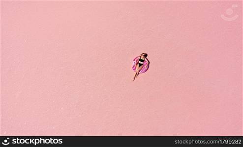 Aerial view of Beautiful woman lying in a bikini on inflatable mattress on pink salt lake. copy space. opening of the tourist season. summer holiday concept. taken from above from a drone.. Aerial view of Beautiful woman lying in a bikini on inflatable mattress on pink salt lake. copy space. opening of the tourist season. summer holiday concept. taken from above from a drone