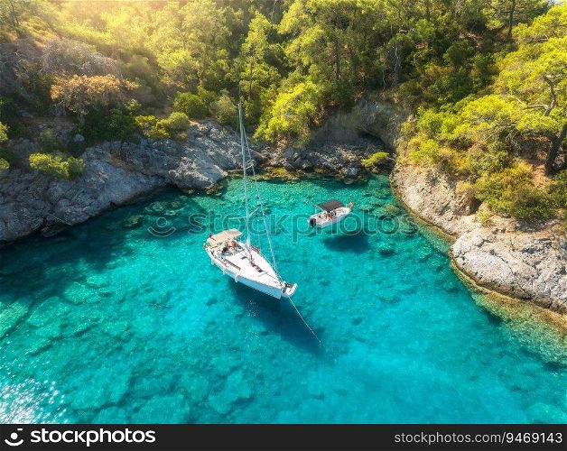 Aerial view of beautiful yacht and sailboat on the sea at sunrise in summer. Oludeniz lagoons, Turkey. Top view of bay, luxury yacht, motorboat, clear blue water, beach, rocks and green trees. Travel