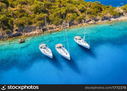 Aerial view of beautiful yachts and boats on the sea at sunset in summer. Gemiler Island in Turkey. Top view of luxury yachts, sailboats, clear blue water, beach, mountain and green trees. Travel