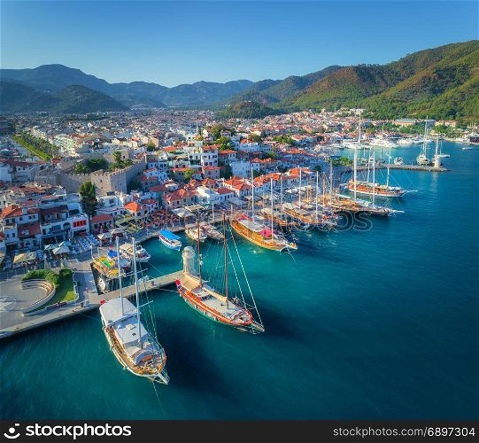 Aerial view of boats and beautiful architecture at sunset in Marmaris, Turkey. Colorful landscape with boats in marina bay, sea, city, mountains. Top view from drone of harbor with yacht and sailboat. Aerial view of boats and beautiful architecture at sunset