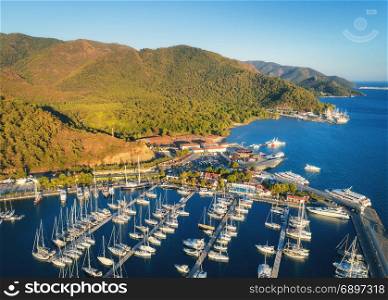 Aerial view of boats and beautiful mountains at sunset in Marmaris, Turkey. Colorful landscape with boats in marina bay, sea, city, forest. Top view from drone of harbor with yacht, sailboat. Travel. Aerial view of boats and beautiful mountains at sunset