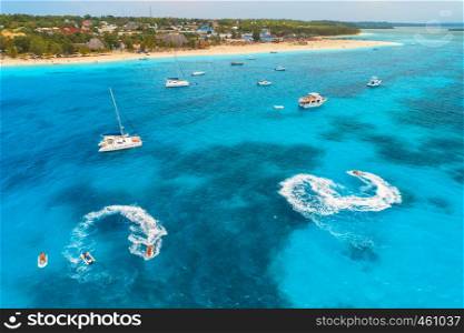 Aerial view of boats and floating water scooter in blue sea at sunset in summer. Holiday in Indian ocean, Zanzibar, Africa. Top view of jet ski in motion. Tropical seascape with moving motorboat
